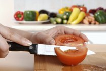 Main Découpage d'une tomate sur un bureau en bois au couteau — Photo de stock