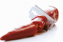A hot chilli with a razor blade on white surface — Stock Photo
