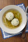Brodo chiaro con verdure e gnocchi in piatto bianco sopra asciugamano con cucchiaio — Foto stock