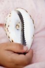 Closeup cropped view of child hand by cowrie sea shell — Stock Photo