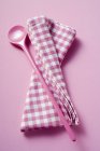 Closeup view of pink cooking spoon and checkered towel — Stock Photo