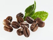 Granos de café tostados con hojas - foto de stock