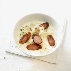 Sauerkraut soup with sausages on white plate over towel — Stock Photo