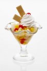 Closeup view of fruit cocktail with cream and wafers in glass on white surface — Stock Photo