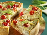 A fennel and tomato tart, partly sliced on wooden desk over green surface — Stock Photo