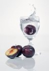 Closeup view of plum falling to glass of water — Stock Photo
