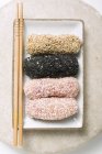 Close-up vista superior de bolinhos revestidos de sementes de gergelim e flocos de coco com pauzinhos em placa retangular — Fotografia de Stock