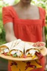 Daytime view of woman holding plate of wraps and salsa — Stock Photo
