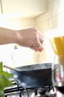 Closeup view of hands adding seasoning ingredients in frying pan — Stock Photo