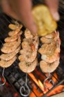 Closeup cropped view of hand squeezing lemon juice over prawn skewers on grill rack — Stock Photo