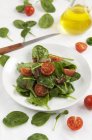 Салат зі шпинату з вишневими помідорами на білій тарілці над скатертиною — стокове фото