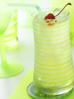 Closeup view of Tom Collins cocktail in a green striped glass with a straw, ice and Maraschino cherry — Stock Photo