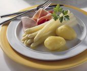 Asparagus with boiled ham, butter and potatoes on plate with cutlery — Stock Photo