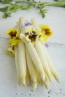 Pealed asparagus with pansies over white wooden surface — Stock Photo