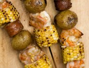 Креветки, кукуруза, колбаса и картофельные кабобы на деревянной поверхности — стоковое фото