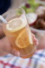 Closeup cropped view of hand holding a glass of iced tea with lemon slices — Stock Photo