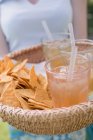 Closeup view of woman serving basket of iced tea and tortilla chips — Stock Photo