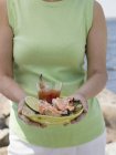Cropped view of woman holding plate of crab claws and dip on beach — Stock Photo