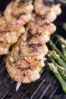 Closeup view of prawn skewers and asparagus spears on barbecue grating — Stock Photo