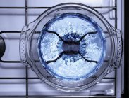 Draufsicht auf blubberndes Wasser in einer Glaspfanne auf einer Gasflamme — Stockfoto