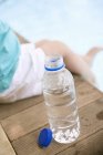 Крупный план ребенка, сидящего рядом с бутылкой воды на краю бассейна — стоковое фото