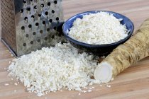 Horseradish, whole and grated with a grater on wooden surface — Stock Photo