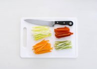 Жюльенские овощи на доске с ножом над белой поверхностью — стоковое фото