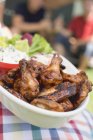 Vista close-up de asas de frango grelhadas e saladas com pessoas no fundo — Fotografia de Stock