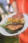 Woman holding plate of grilled salmon — Stock Photo