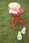 Colored paper cups and plates on folding stool in garden — Stock Photo