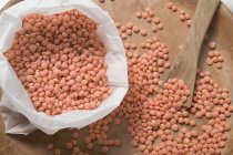 Closeup top view of red lentils on wooden plate and in bag — Stock Photo