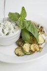 Fried courgettes with basil and herb quark on white plate with bowl — Stock Photo