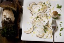 Elevated view of cep nushroom Carpaccio on chopping board and whole ceps — Stock Photo