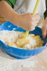 Vista de primer plano del niño mezclando huevo con harina y mantequilla en un tazón - foto de stock