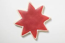 Vista de cerca de la galleta en forma de estrella con glaseado rojo en la superficie blanca - foto de stock
