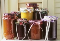 Vista de cerca de mermeladas y salsas en frascos atados con cintas - foto de stock