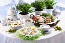 Вкусный пасхальный завтрак на столе с яйцами, мясом и растениями в горшках — стоковое фото