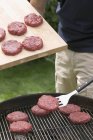 Uomo che mette hamburger crudi sulla griglia — Foto stock