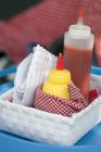 Bottle of ketchup, mustard and paper napkins in basket — Stock Photo