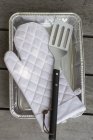 Верхний вид на белый барбекю перчатки и лопатки на алюминиевый лоток — стоковое фото