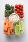 Assorted vegetables with dip in plastic tray on white surface — Stock Photo