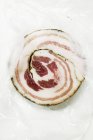 Closeup top view of a Pancetta slice on plastic food wrap — Stock Photo