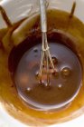 Vista de primer plano de la salsa de chocolate con batidor en un tazón blanco - foto de stock