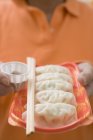 Person holding Wontons with chopsticks on plastic tray and sauce bowl — Stock Photo