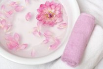 Vista superior de pétalas de flor rosa em tigela de água com toalhas ao lado — Fotografia de Stock
