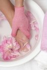 Повышенный вид на мытье женской ноги в успокаивающей ванне с лепестками цветов — стоковое фото