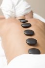Mujer acostada teniendo terapia de LaStone con hilera de piedras negras en la espalda - foto de stock
