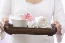 Frau hält Handtücher mit Schale und Orchidee auf Tablett — Stockfoto
