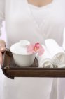 Donna che tiene asciugamani con ciotola e orchidea sul vassoio — Foto stock