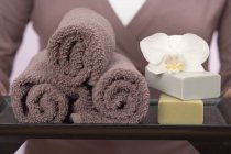 Frau hält Handtücher, Seifen und Orchideen auf Tablett — Stockfoto